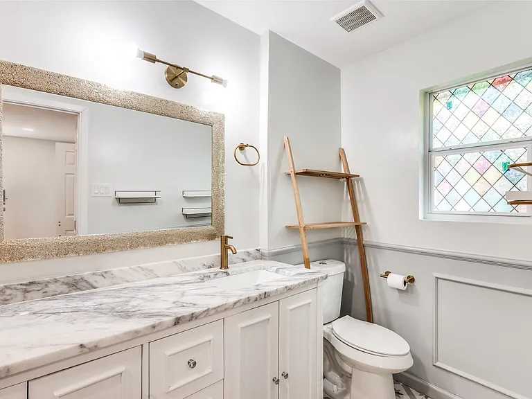 Bathroom featuring a spacious vanity with white cabinetry and a marble countertop, oversized mirror with textured frame, and a stained glass window