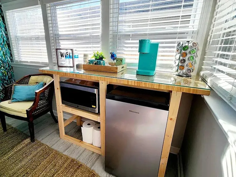 Sunlit beverage nook with counter space, mini fridge, microwave, and coffee/tea station set by corner windows.
