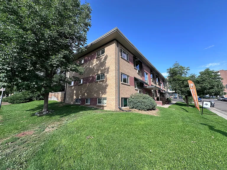 Charming brick apartment building surrounded by lush greenery and clear skies, offering a serene residential environment.