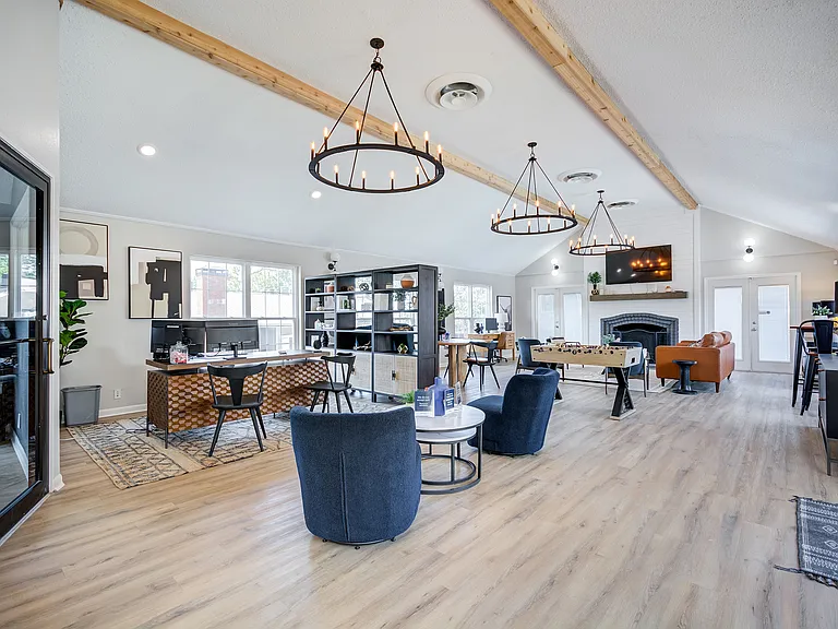 A lofted clubhouse and leasing office are shown with comfortable seating areas, professional workspace, and foosball table at ReNew on Cantrell.