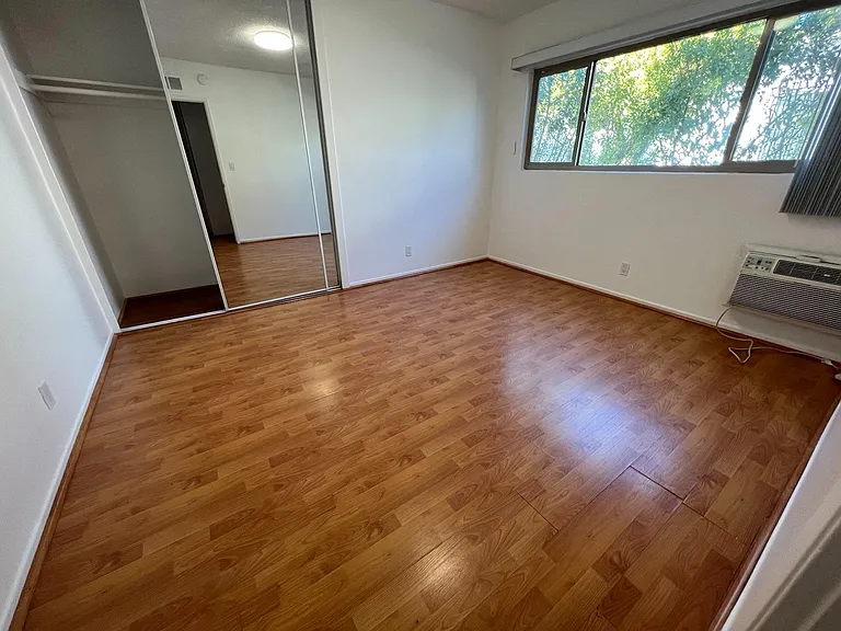 Primary bedroom with: floor-to-ceiling mirrored wardrobe, wall-mounted aircon, and peaceful aspect onto greenery. Perhaps this room could be a ballet rehearsal studio... (thinking out loud).