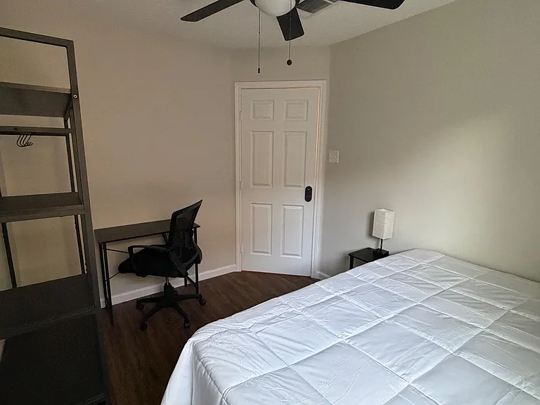 Furnished bedroom with a ceiling fan, comfortable bed, and dedicated desk area for work or study.