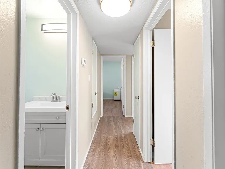 Hallway leading to guest bathroom and bedrooms, featuring a large closet, linen storage, fresh paint, and beautiful hardwood flooring.