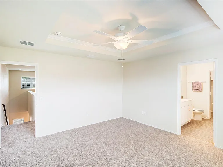 Carpeted interior space featuring a tray ceiling with a ceiling fan