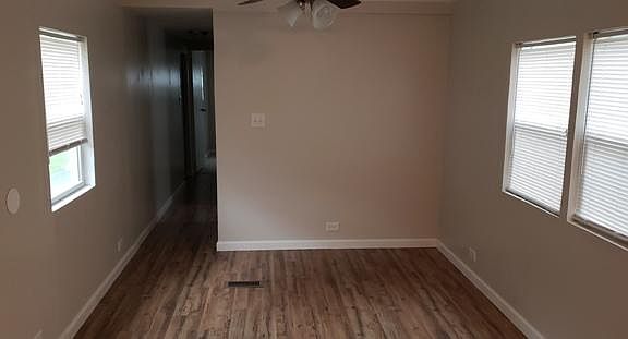 This is the living room which has several windows, ceiling fan and pre fab wood flooring.