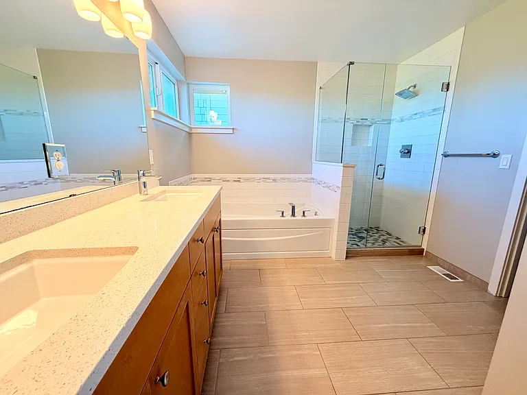Upgraded primary bathroom with quartz countertops, tiled shower and frameless shower glass.