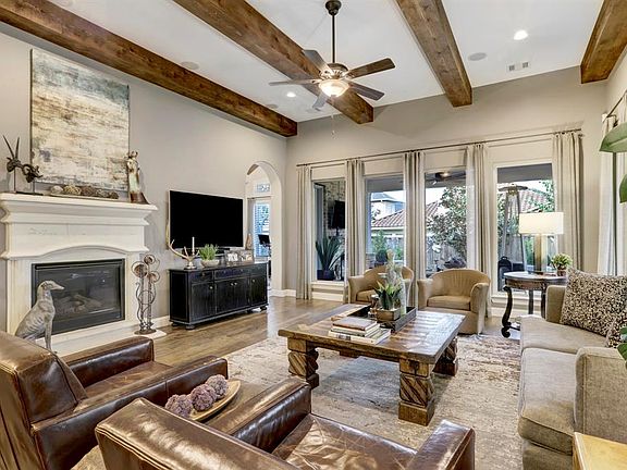 Beautiful living area with fireplace and rich wood ceiling beams with open view to covered outdoor patio