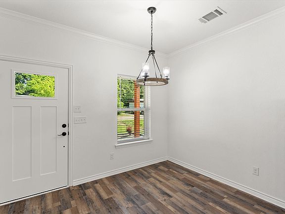 Bright room featuring a paneled entry door with a rectangular lite, wood-finish flooring, and a multi-light chandelier