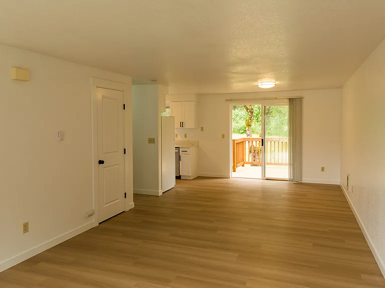 Bright open-concept living and dining area with updated flooring, freshly painted walls, and sliding door access to the private backyard deck.