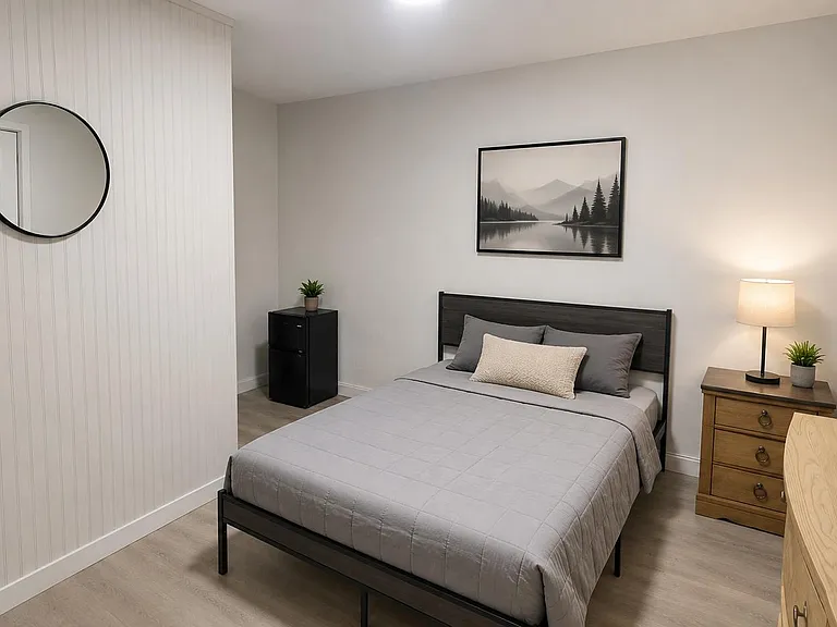 Furnished bedroom with full bed, nightstand lighting, dresser, and TV setup, plus neutral finishes for easy move-in.