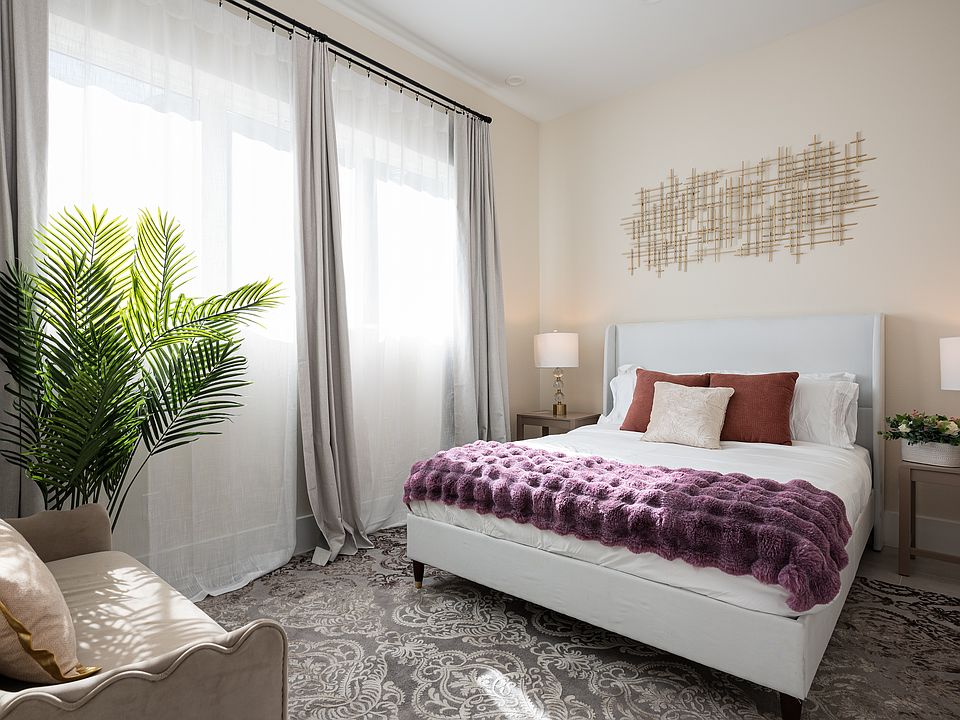 A cozy bedroom with a queen size plush bed, a large window with blackout curtains, touch of greenery.