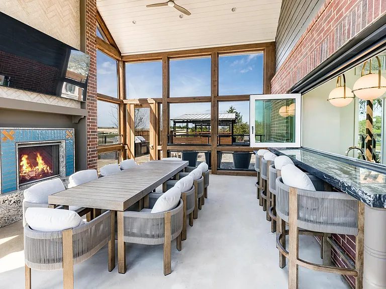 Screened-in porch with a harvest dining table, an adjacent catering kitchen and entertainment lounge inside, plus a cozy outdoor fireplace.