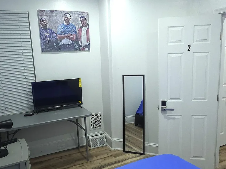 Private bedroom with wood-look flooring, overhead lighting, and a work desk; includes a full-length mirror and TV.