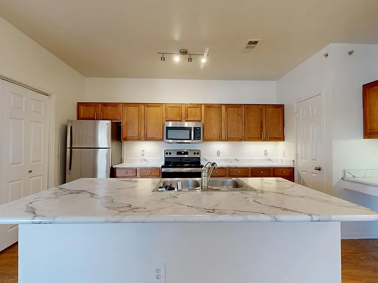Apartment kitchen with stainless steel appliances, wood-style flooring, and marble-style countertops (shown here). Quartz-style countertops are available in select homes.