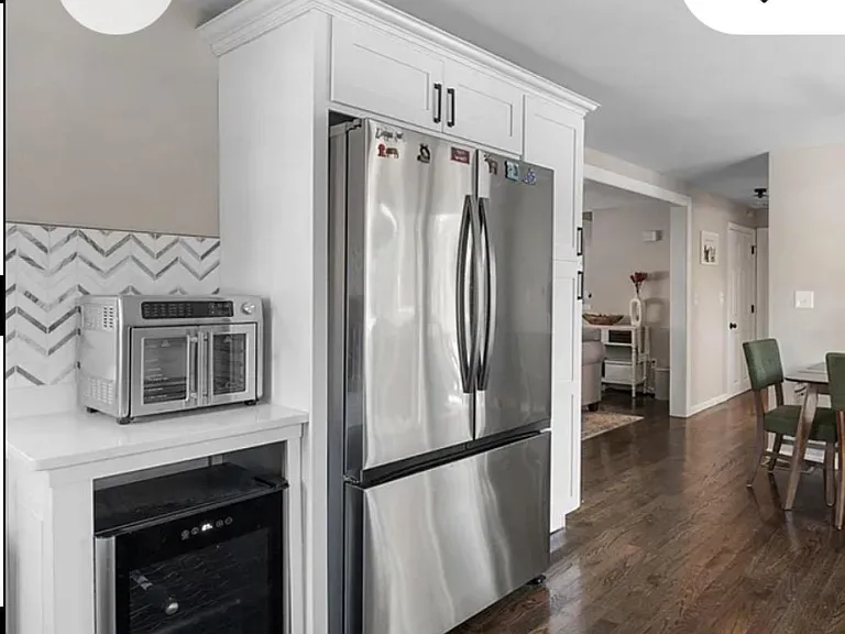 Kitchen features tall white cabinetry, stainless French-door fridge, and a dedicated beverage station with wine fridge.