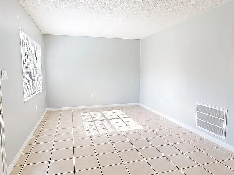 Bright and inviting room with large window, neutral tile flooring, and ample natural light.