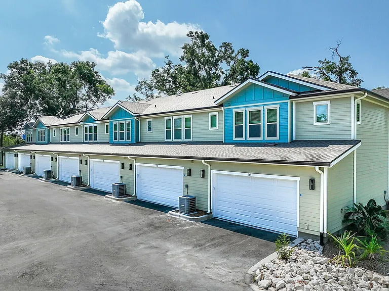 Charming townhouse row with vibrant blue accents, highlighting a serene suburban setting with spacious garages and lush trees.