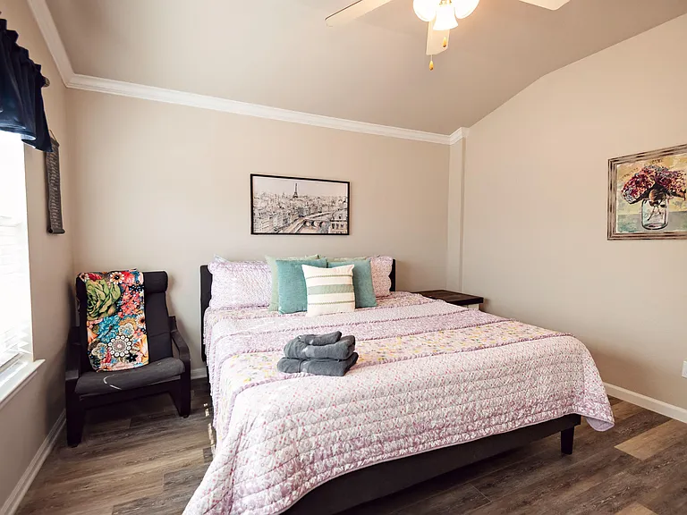 Bedroom with a full bed, side table, armchair seating, and a window with blinds for natural light and privacy.