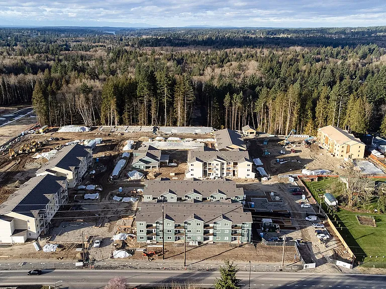 Wide aerial of construction at The Elowen in Lacey WA. New apartment homes taking shape among the towering evergreen trees on a bright Pacific Northwest day.