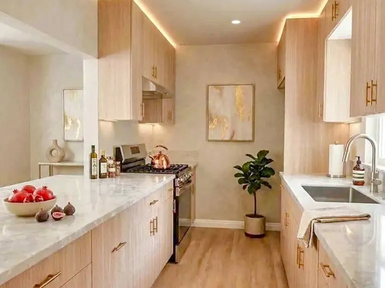 Brand-new kitchen with light wood cabinetry, gold-toned hardware, stone-look countertops, and updated lighting.