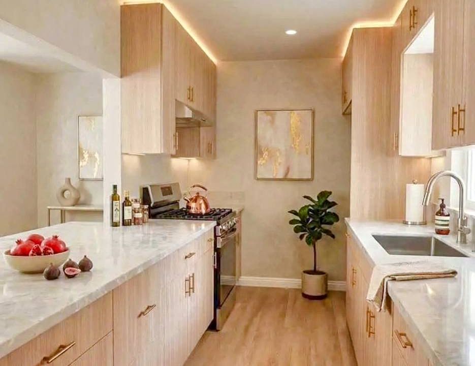 Brand-new kitchen with light wood cabinetry, gold-toned hardware, stone-look countertops, and updated lighting.