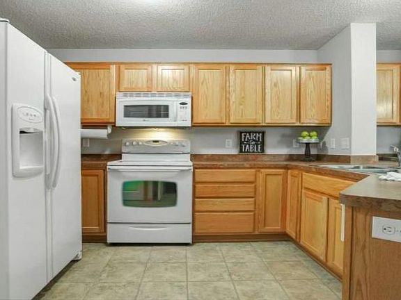 Kitchen showing peninsula with sink refrigerator, stove/microwave with light oak cabinetry.