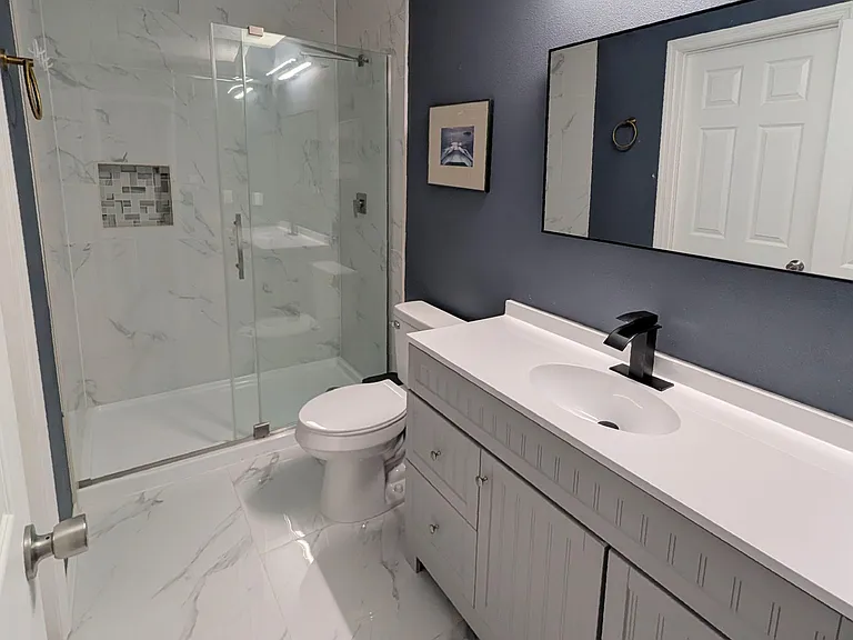 Updated bathroom with glass-enclosed shower, large vanity with storage, and marble-look tile flooring.
