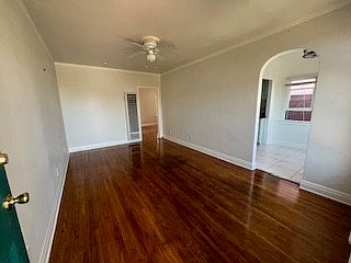 The other side of the living room that leads to the kitchen on the right and bedroom on the other side. Heater and fan in this room. Crown molding and wood flooring.