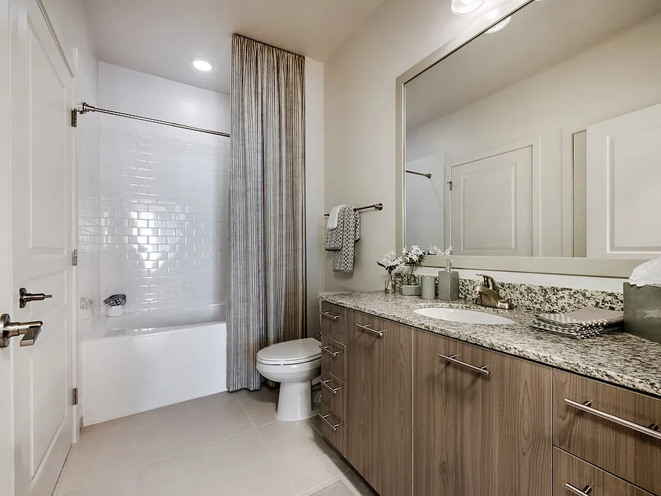 Bath with granite countertops, brown cabinetry, hard surface flooring and tiled bathtub