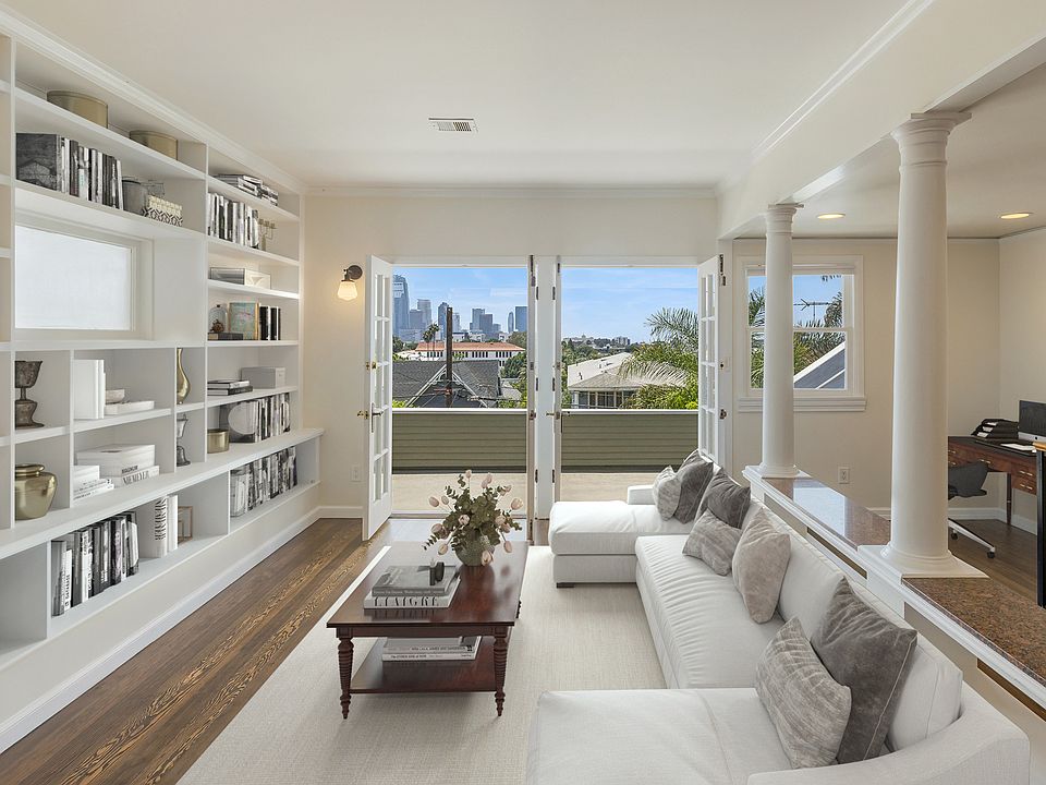 Living room with built in shelving, skyline views, private patio shown with example staging. Unit comes unfurnished