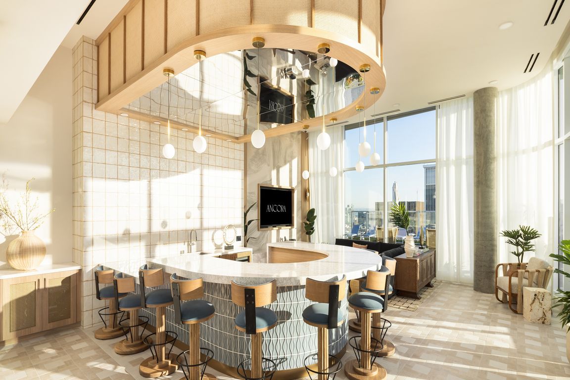 Luxurious modern kitchen with a unique curved island, elegant bar stools, and expansive floor-to-ceiling windows offering stunning city views.
