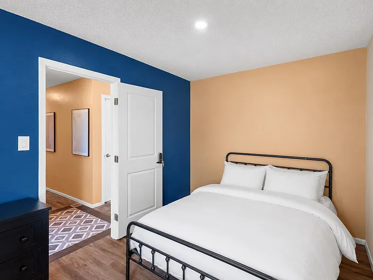 Private bedroom with a full bed, wood-style floors, and a bedside dresser, plus easy access to the adjacent hallway.