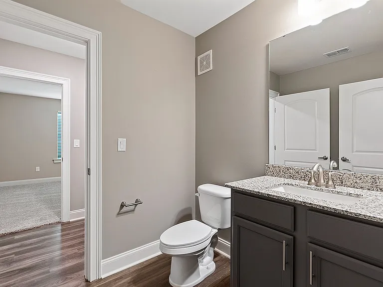 Modern bathroom with elegant granite countertop, sleek fixtures, and a view into a cozy, carpeted bedroom.