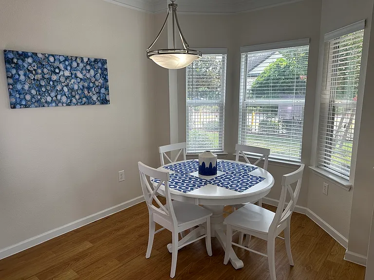 Bright and inviting dining nook with elegant chandelier, featuring a round white table set for four, accented by blue decor and large windows providing a scenic view. Bright and inviting dining nook with elegant chandelier, featuring a round white table s