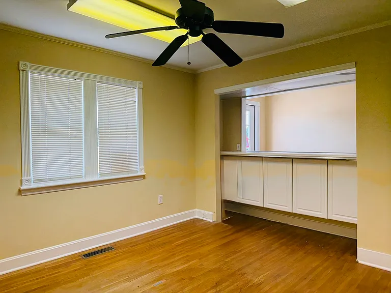 Front desk adjacent reception room with warm walls, ceiling fan and hardwood floors, featuring built-in storage for hospitality supplies, ideal for visitor waiting or small private meetings.