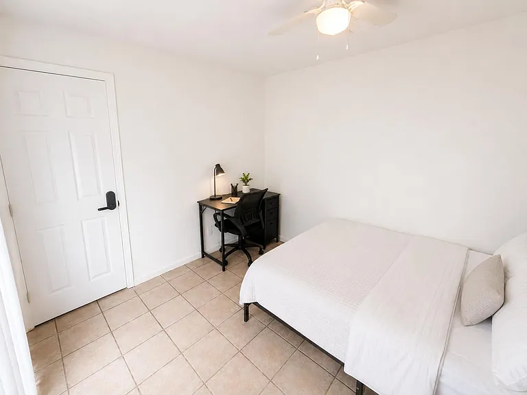 Furnished bedroom with tile flooring, ceiling fan, and a dedicated desk/workstationideal for studying or remote work.