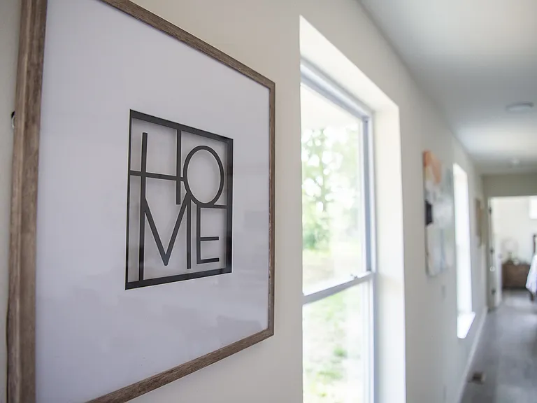 Inviting hallway with large windows, natural light, and a stylish 'HOME' art piece, leading towards a cozy room.