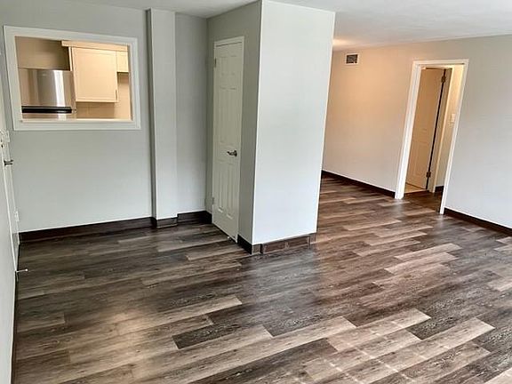 The living room view of the 2-bed floorplan facing the kitchen and dining room with plank flooring. The doorway on the right goes to the bedrooms and bath. The closed door is the entry closet.