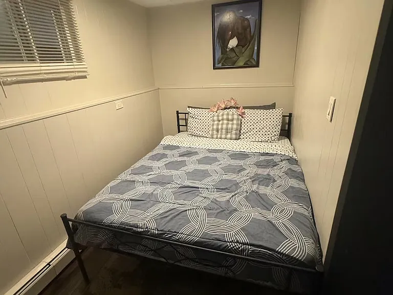 Furnished bedroom with a full-size bed, window with blinds, and durable flooring in a space-efficient layout.