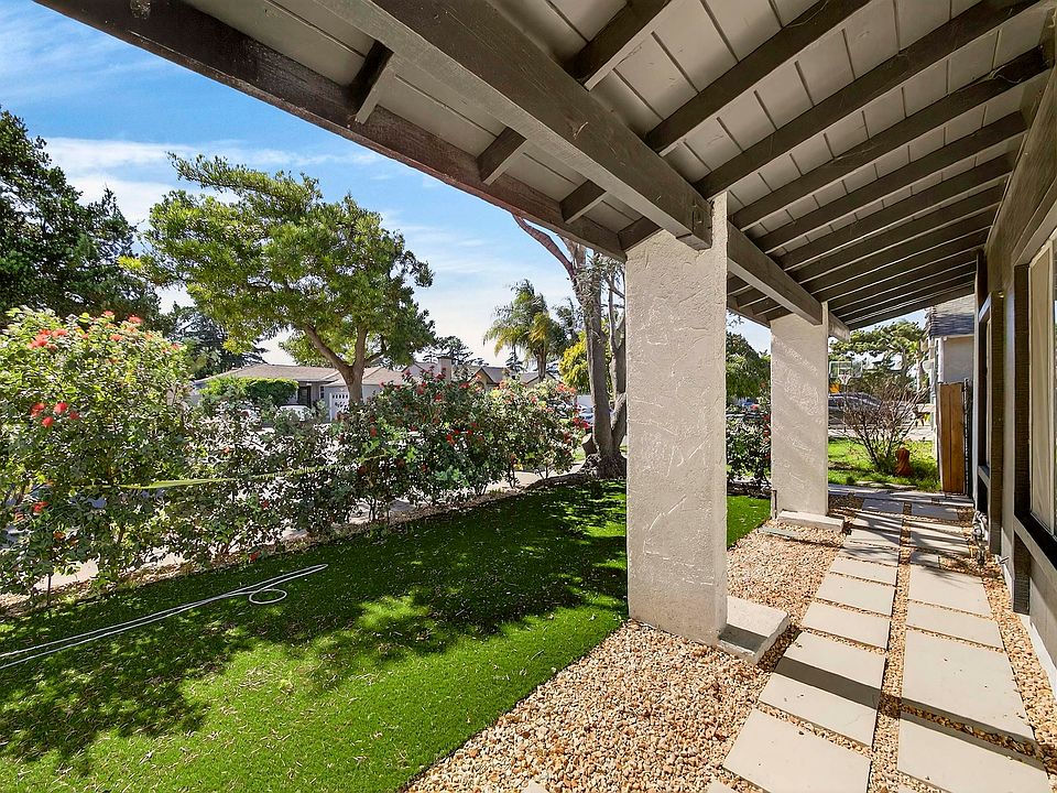 The exposed beam overhang and stucco columns frame a manicured front lawn, with established flowering hedge offering seclusion from the streetscape.