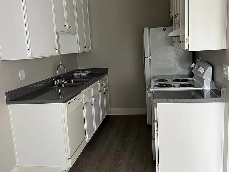 Kitchen with plank style flooring, spacious whit cabinets, dishwasher, refrigerator, and electric stove/oven at IKARIA Apartments in Santee, California.