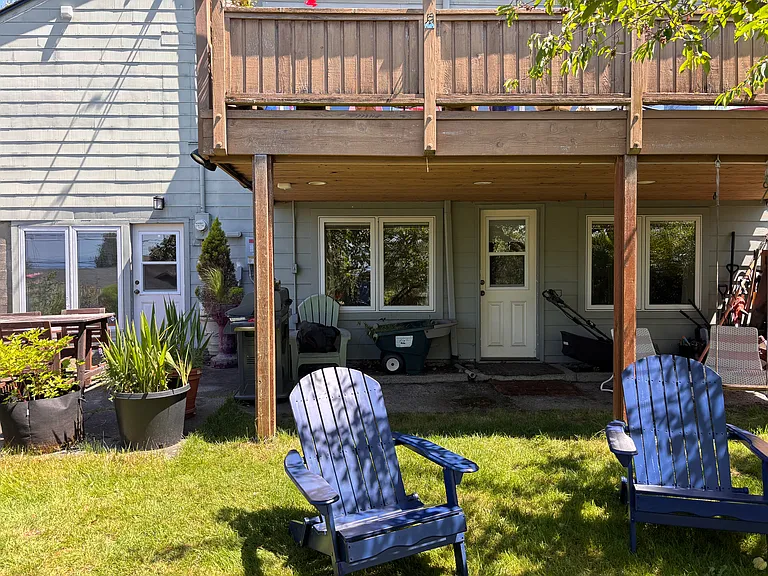 Backyard entrances to apartment, concrete patio with table and grill to left, covered patio area under deck to right