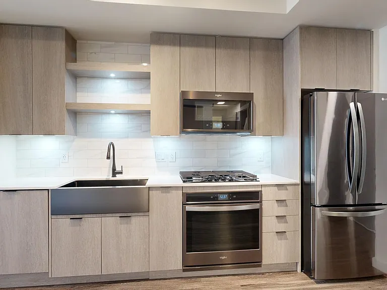Apartment kitchen with black stainless steel appliances, quartz countertops, wood-style flooring, and custom Italian cabinetry.