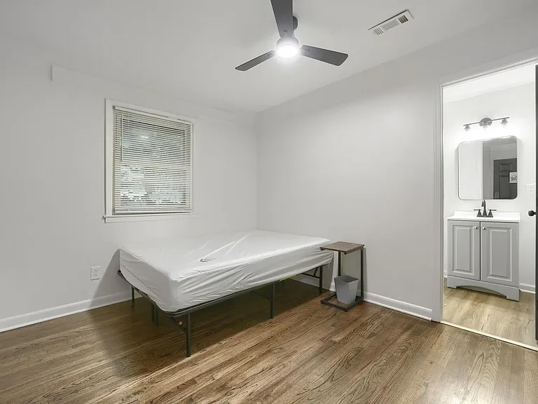 Private bedroom with hardwood floors, ceiling fan, and a window, plus convenient access to a nearby vanity area.