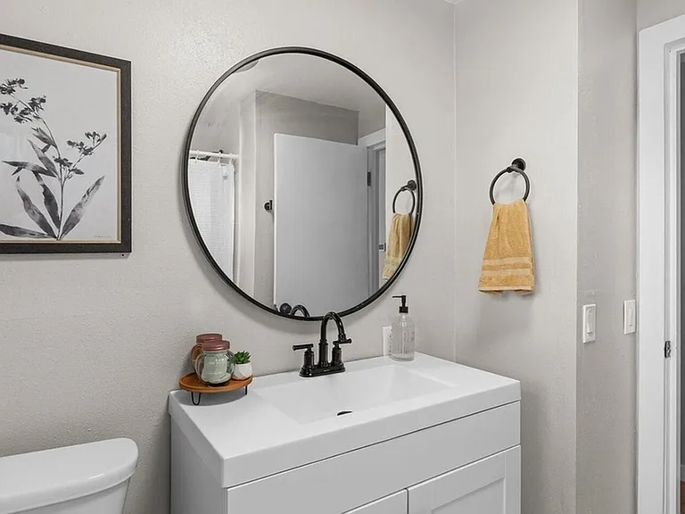 Updated bathroom vanity with generous counter space, round mirror, and convenient towel storage near the shower area.