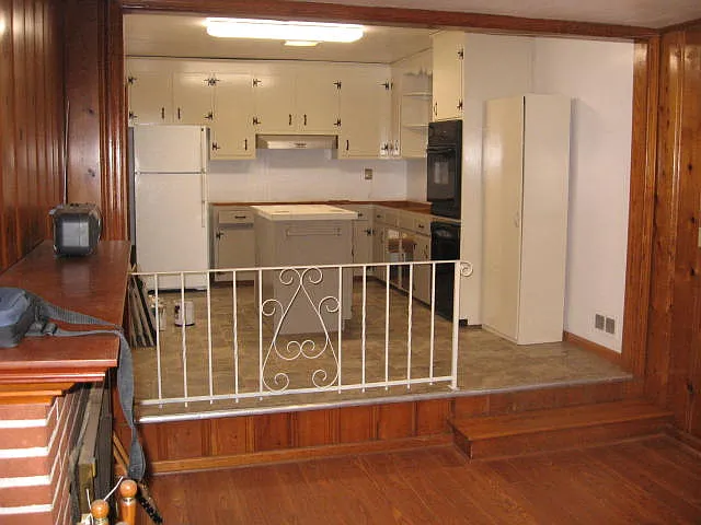 This picture shows the kitchen and adjacent sunken family room with decorative fireplace. The wood paneling has been painted.