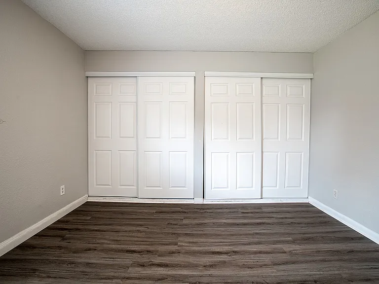 Elegant room with sleek laminate flooring and dual white sliding closet doors, offering ample storage space.