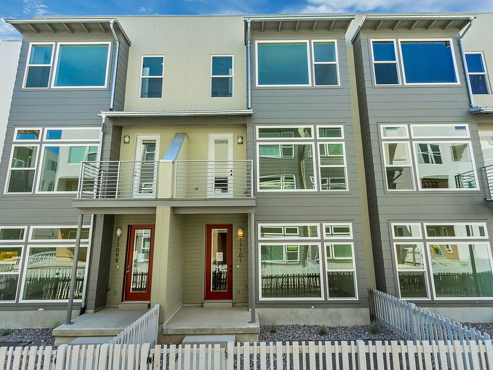 A modern, three-story townhouse with large windows, two red front doors, balconies, and a white pick
