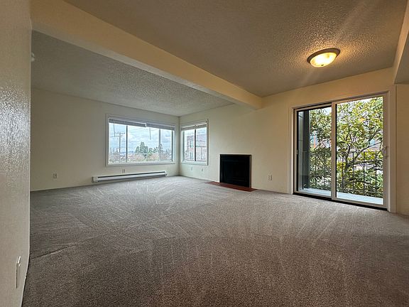 Large living room with balcony slider and large windows overlooking park across the street and Elliott Bay in the distance