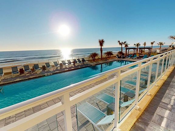 Luxurious beachfront pool with lounge chairs, overlooking the ocean at sunrise